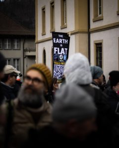 A protest with a person holding a sign that says, "The Earth is Flat"